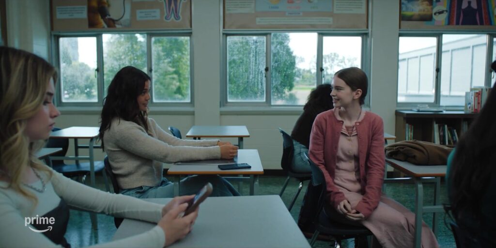 Carrie White zit glimlachend in een klaslokaal tussen klasgenoten in de trailer van de serie Carrie