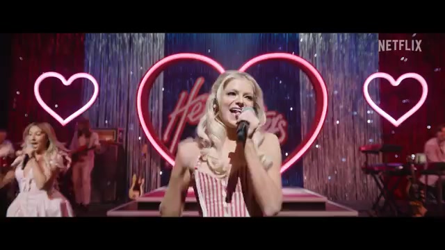 Een countryzangeres op een podium met roze neonharten in de trailer van Heartland