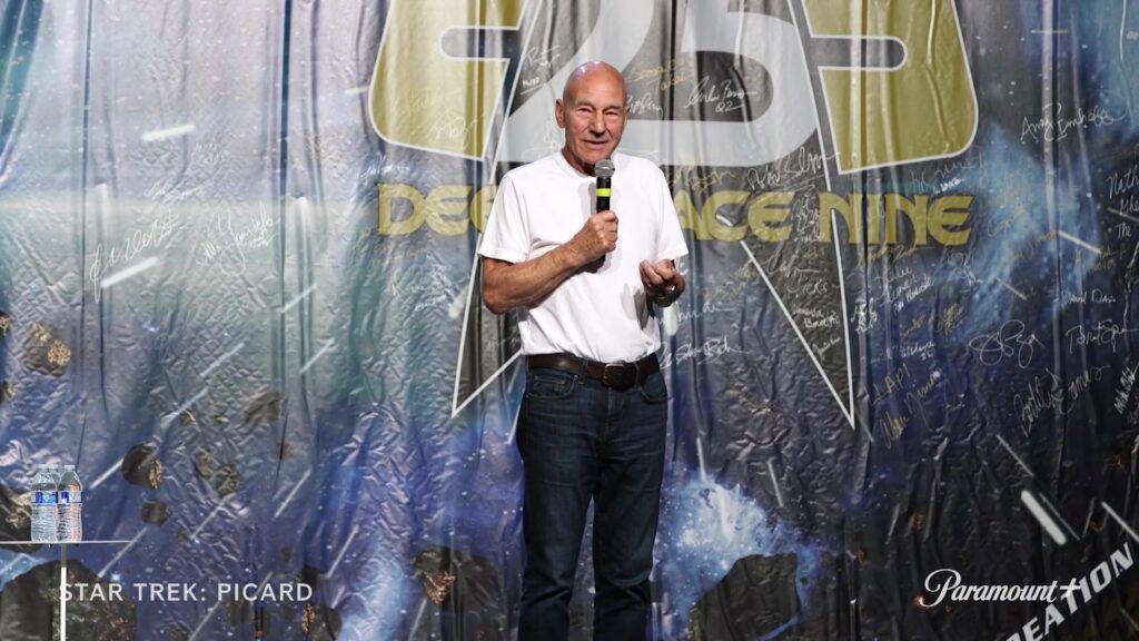 Patrick Stewart met een microfoon op het podium tijdens een Star Trek-conventie, still uit een video van Star Trek