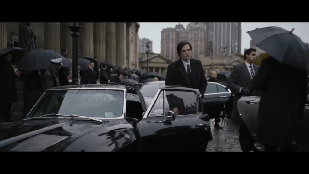 Robert Pattinson als Bruce Wayne bij een zwarte auto in de regen in The Batman