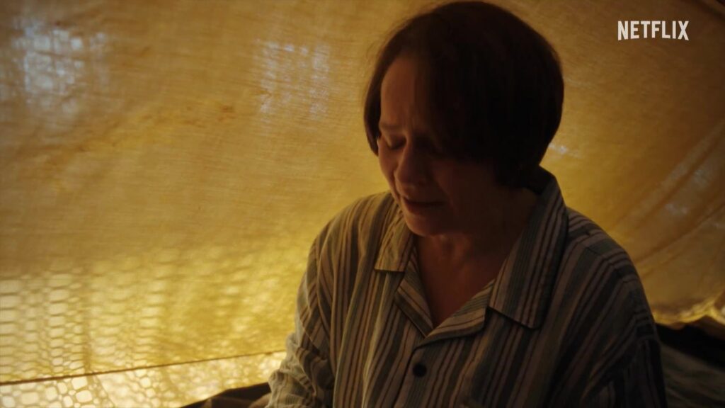 Lies Visschedijk als Toos van der Valk in gevangenschap achter een geel gordijn, still uit de officiële trailer van Toos