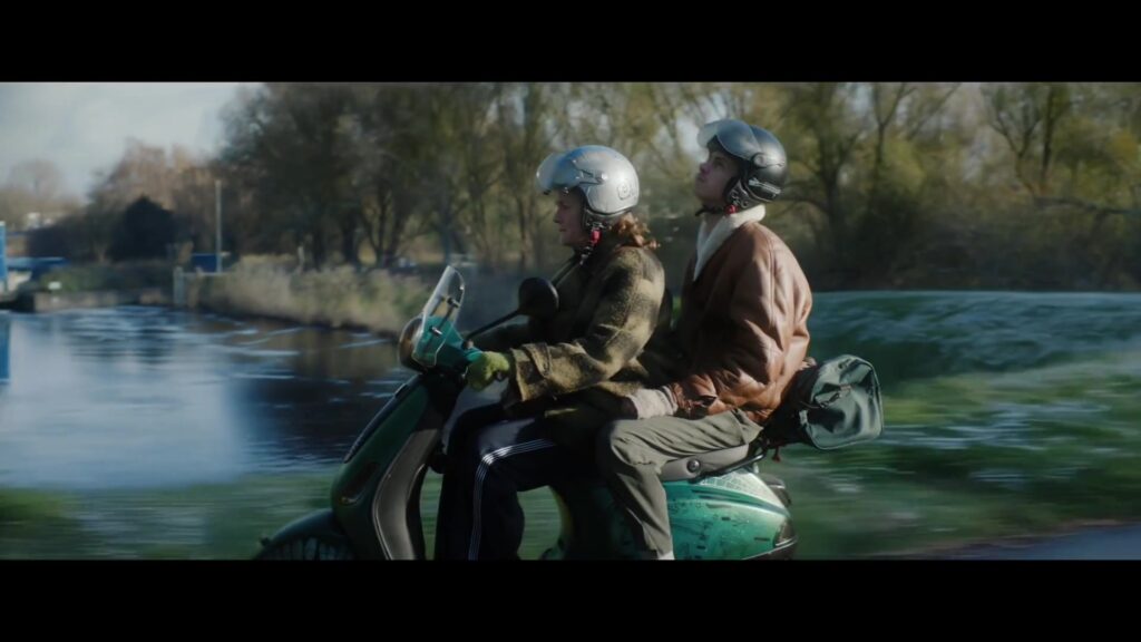 Twee mensen achterop een scooter langs het water in de film Wen er maar aan